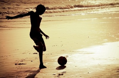 Silhouette of boy on the beach playing football